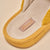 Mustard-yellow slipper close-up showing fabric label and embossed sole reading 'Brunch'.