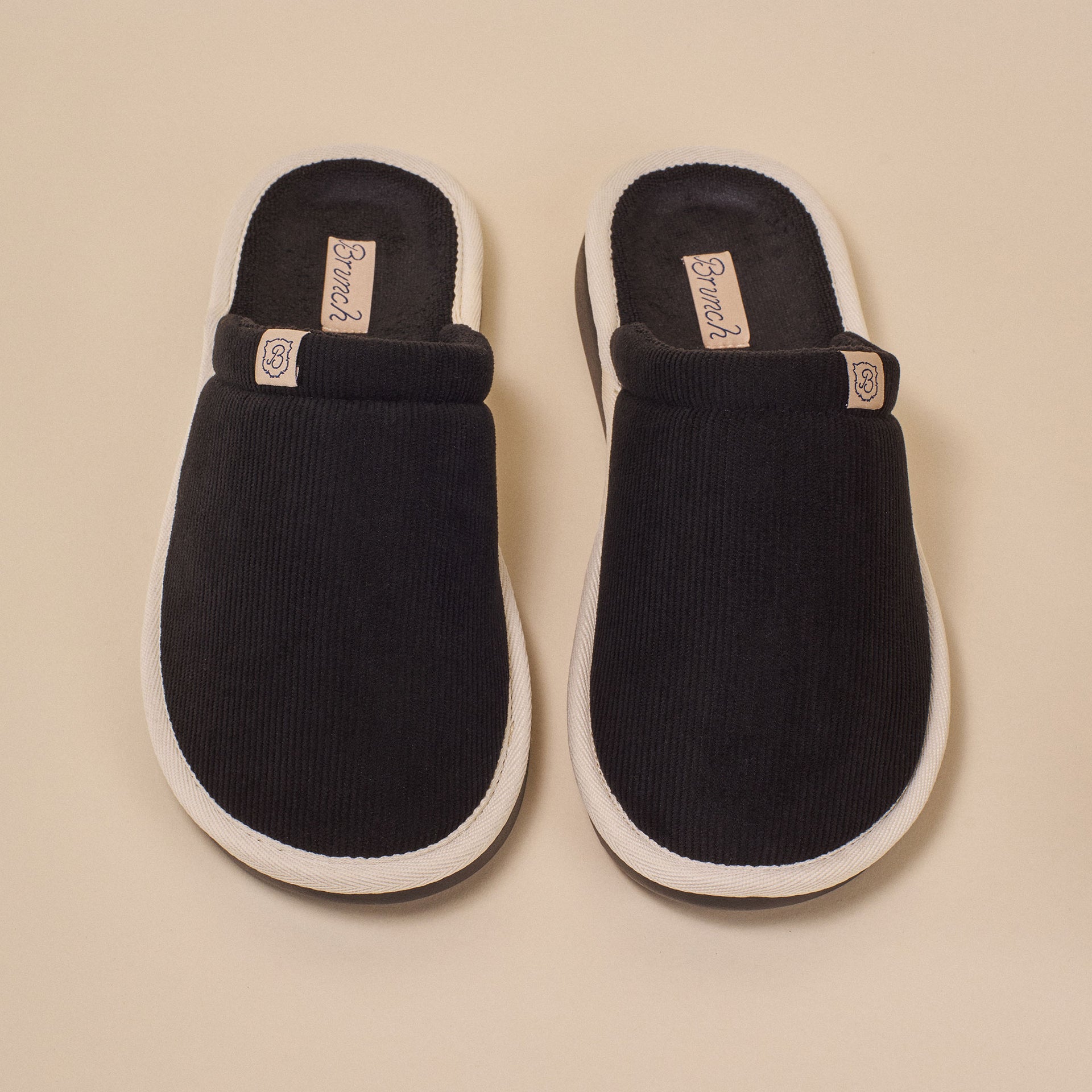 Black corduroy slip-on slippers with white trim, insole label 'Brunch' and small 'B' logo