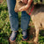 Person in jeans wearing navy clogs that say AMBER WAVES FARM, petting a goat by their legs