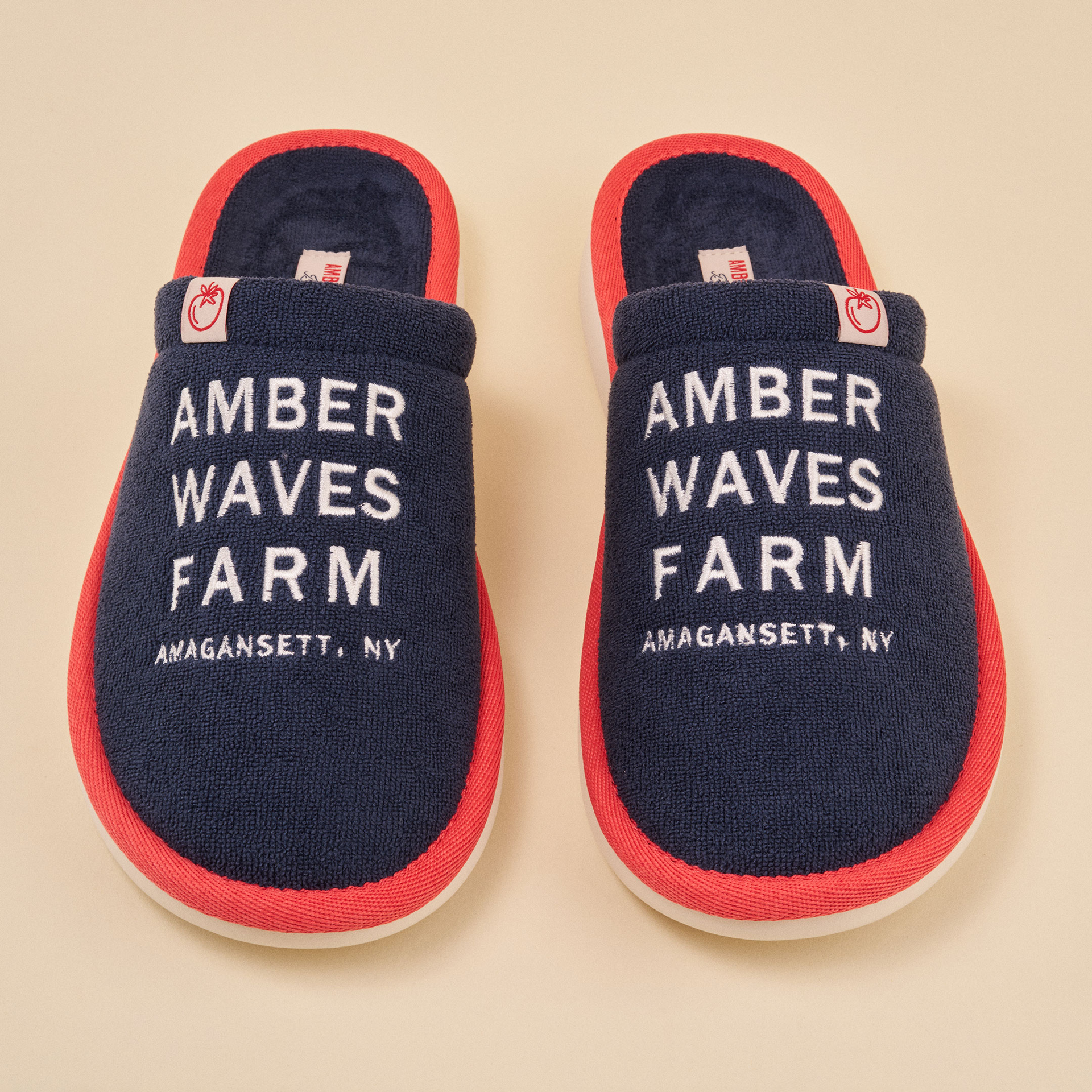 Navy terry slippers with red trim embroidered 'AMBER WAVES FARM AMAGANSETT, NY'.