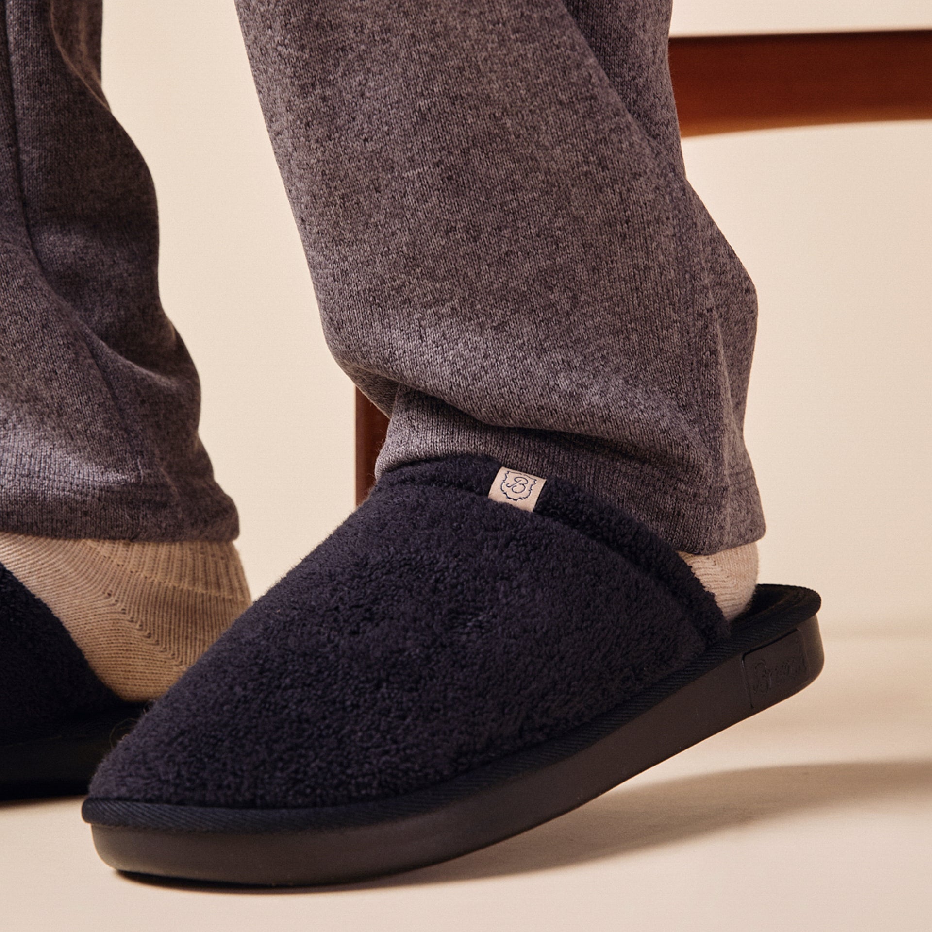 Navy fleece slip-on slipper worn with light socks and gray sweatpants, close-up on foot and sole