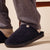 Navy fleece slip-on slipper worn with light socks and gray sweatpants, close-up on foot and sole