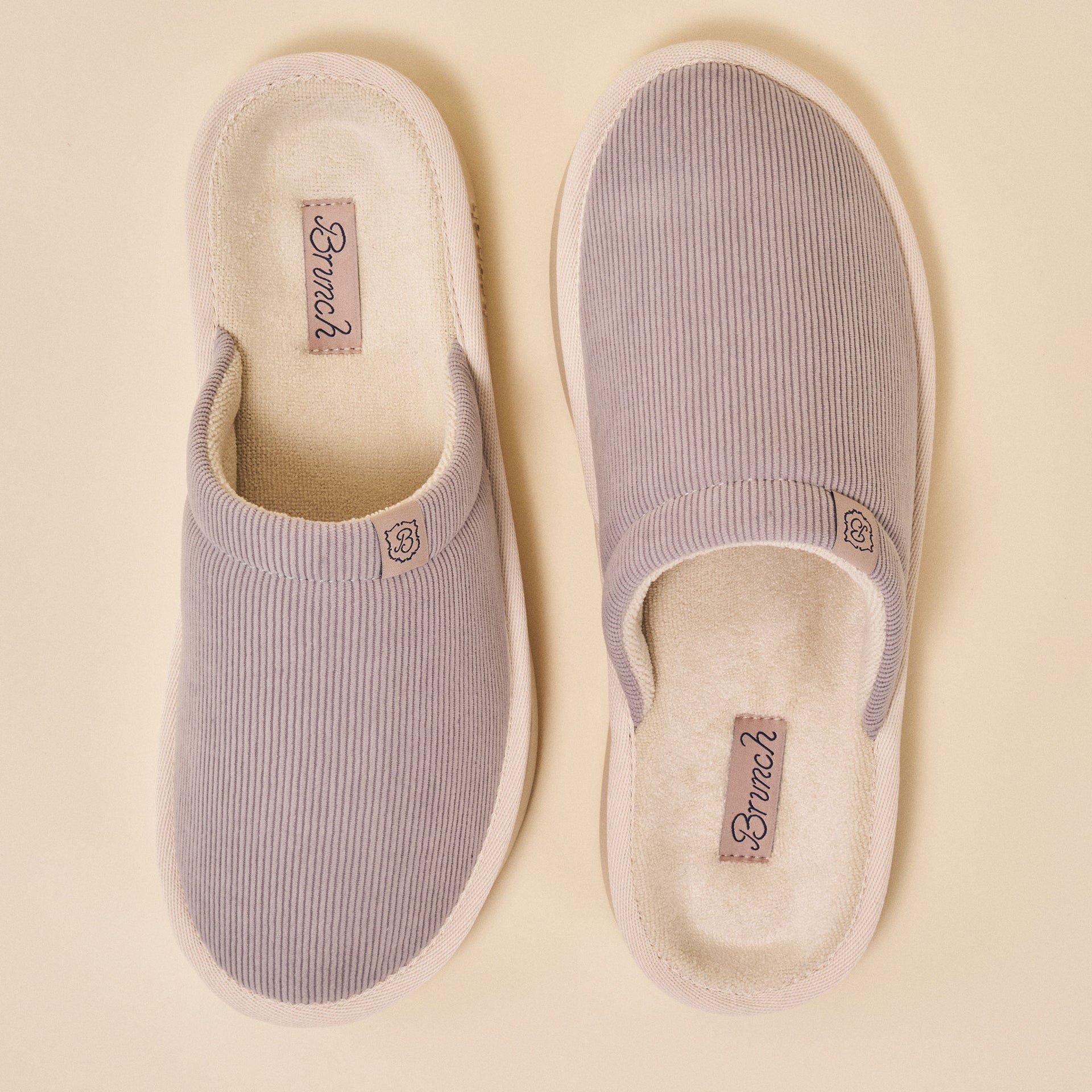 Pair of ribbed grey slip-on house slippers, top view; insole tags read 'Brunch'.