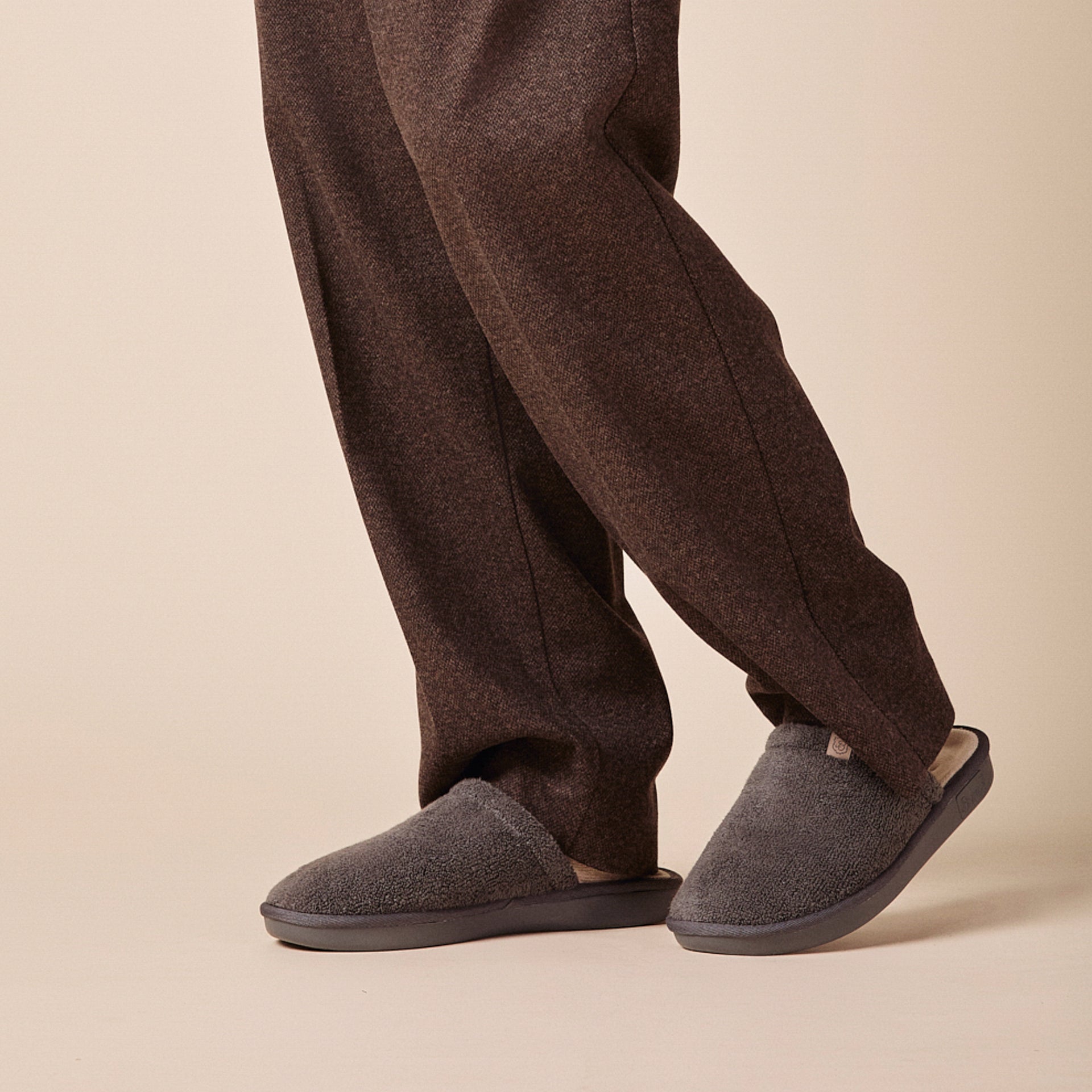 dark gray terry slip-on slippers worn with brown trousers, low-profile sole