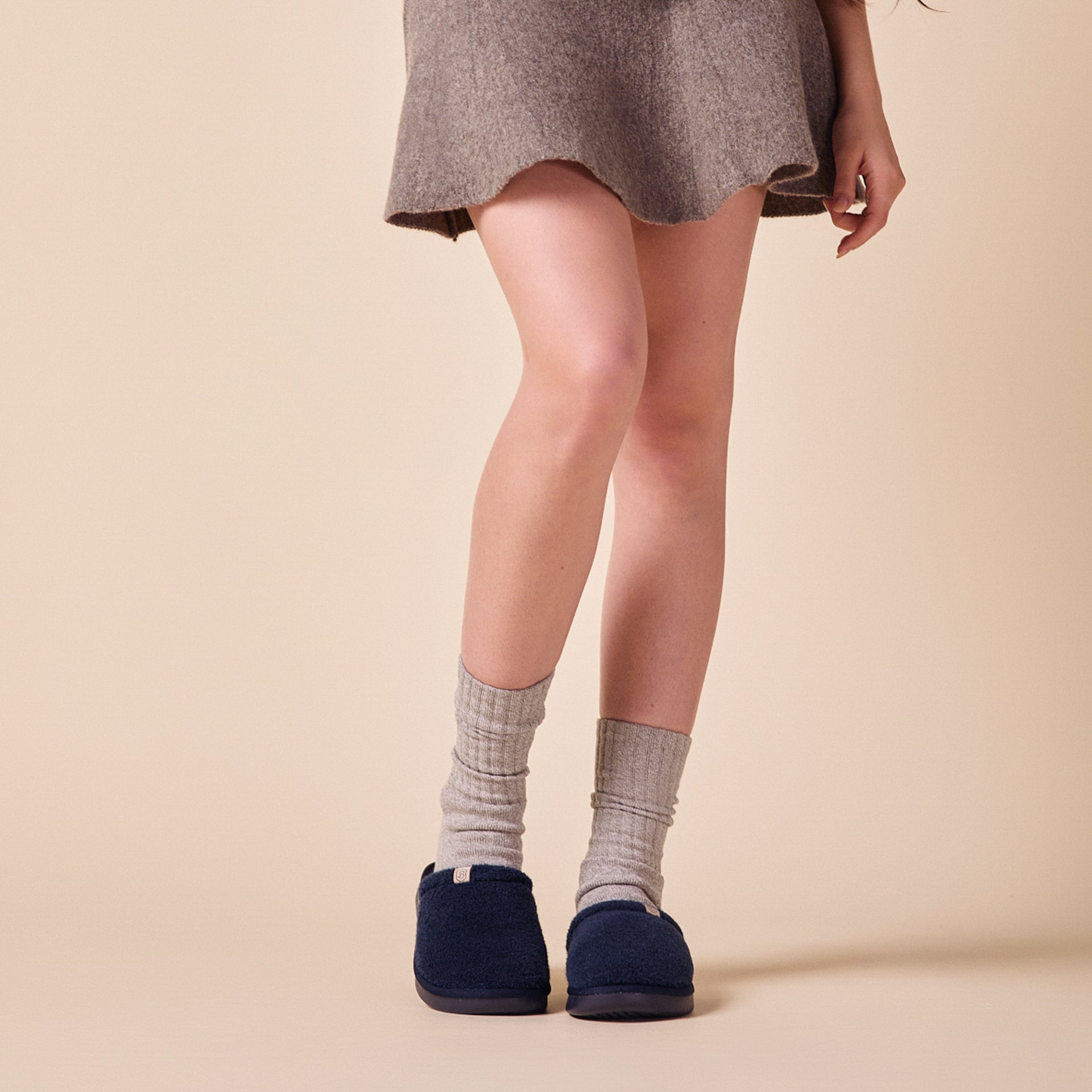 Lower legs wearing gray ribbed socks and navy slip-on fleece slippers; short wool skirt hem visible.