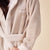 Beige terry robe, belted at waist, embroidered "B" crest and "Brunch" on chest, model's hand holding belt.
