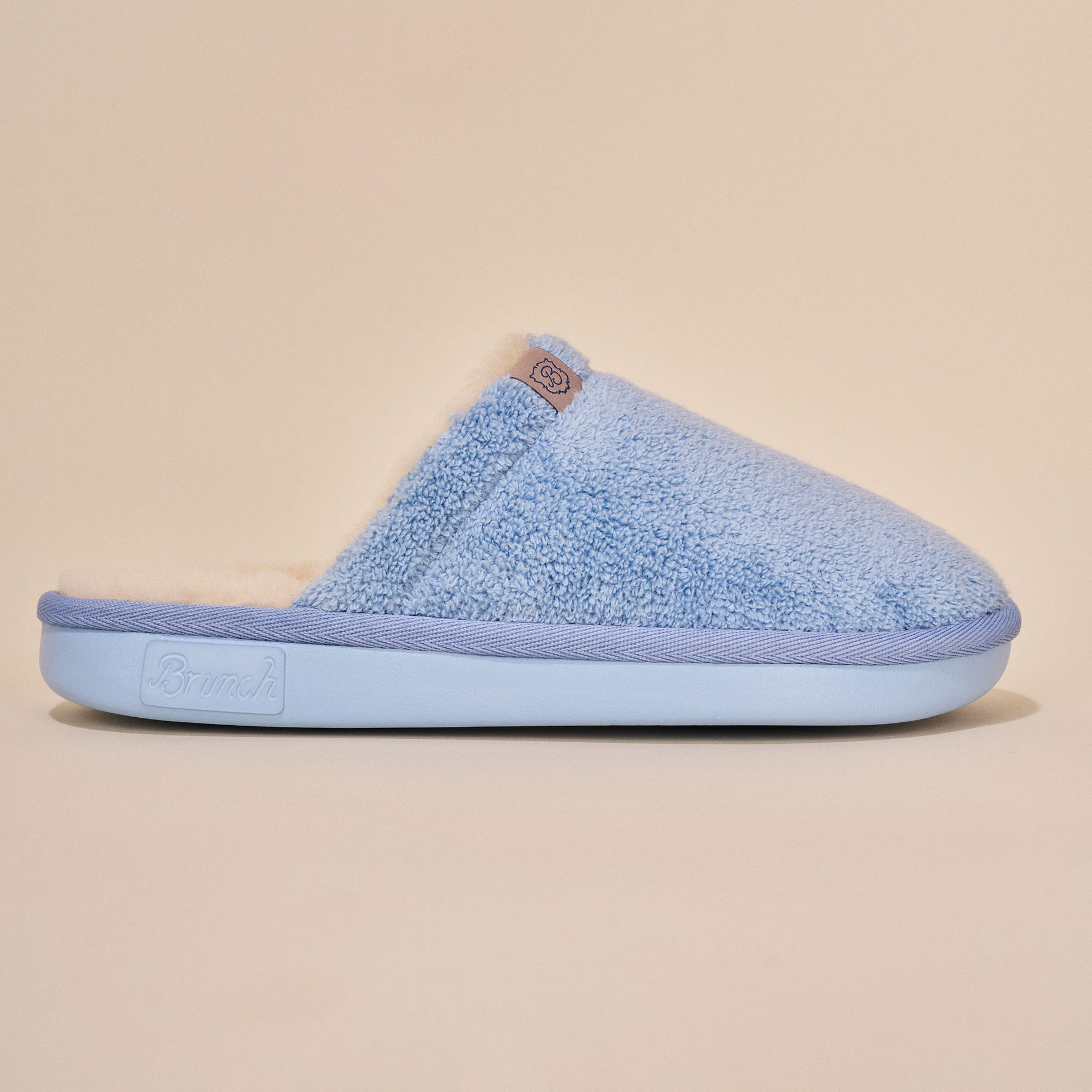 Powder-blue plush slip-on slipper, side view; Brunch logo embossed on sole