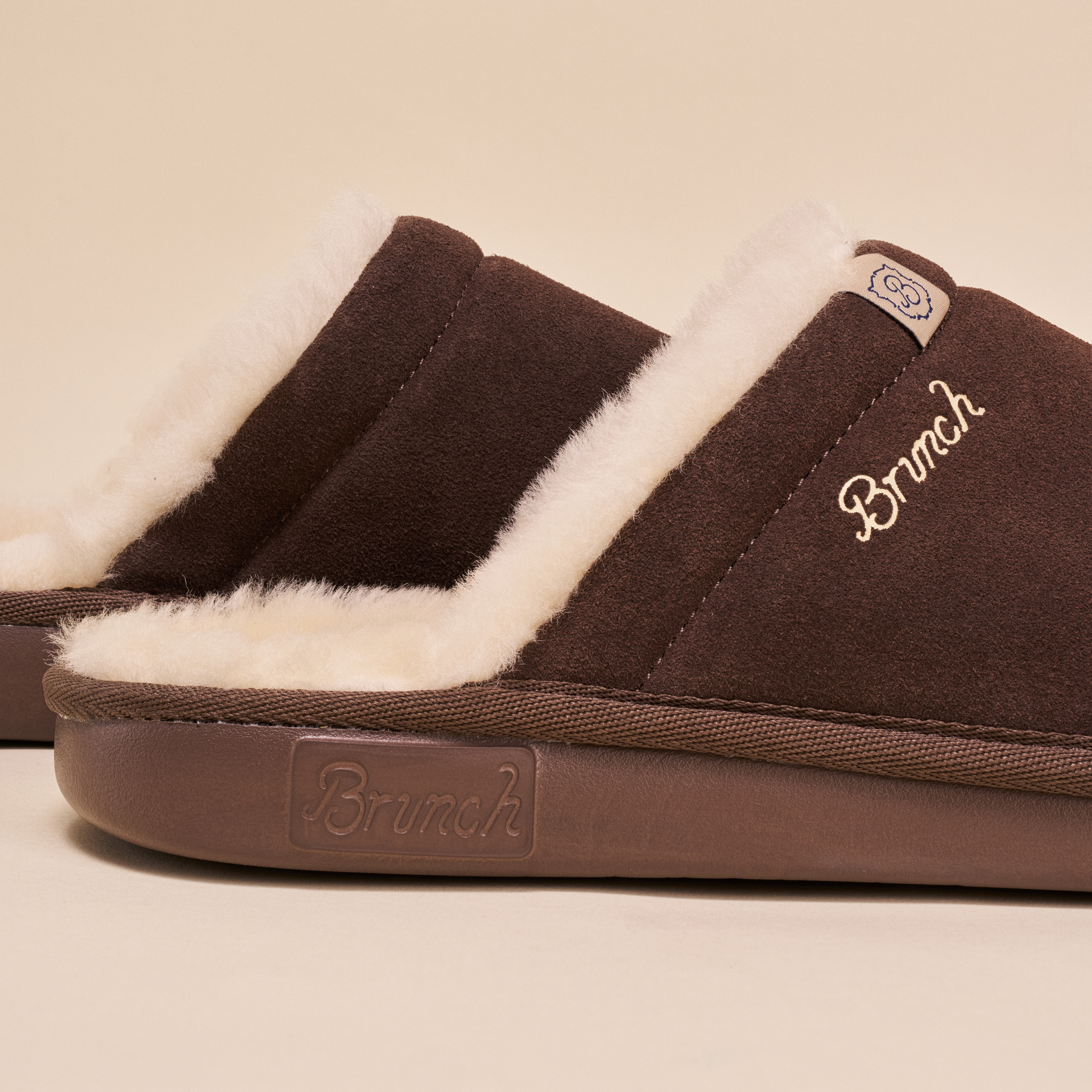 Brown suede slip-on slippers with cream shearling trim and embroidered "Brunch" logo