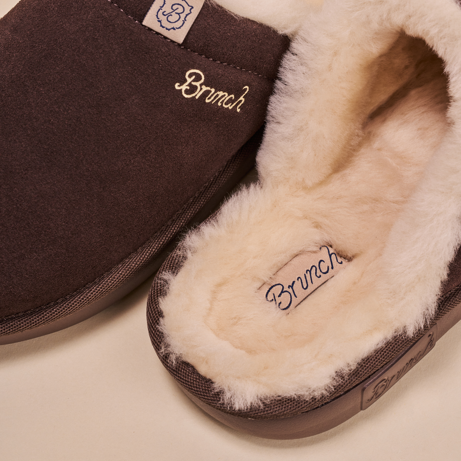 Brown suede slippers with cream shearling lining, embroidered 'Brunch' and small 'B' logo on the heel.