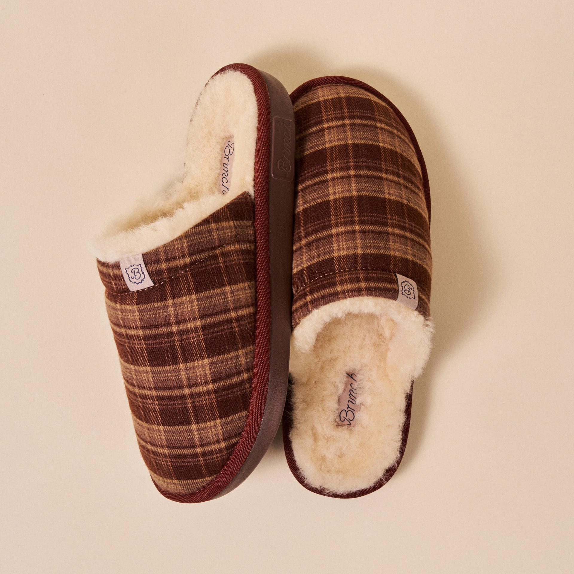 Brown plaid slip-on slippers with cream shearling lining, top view.