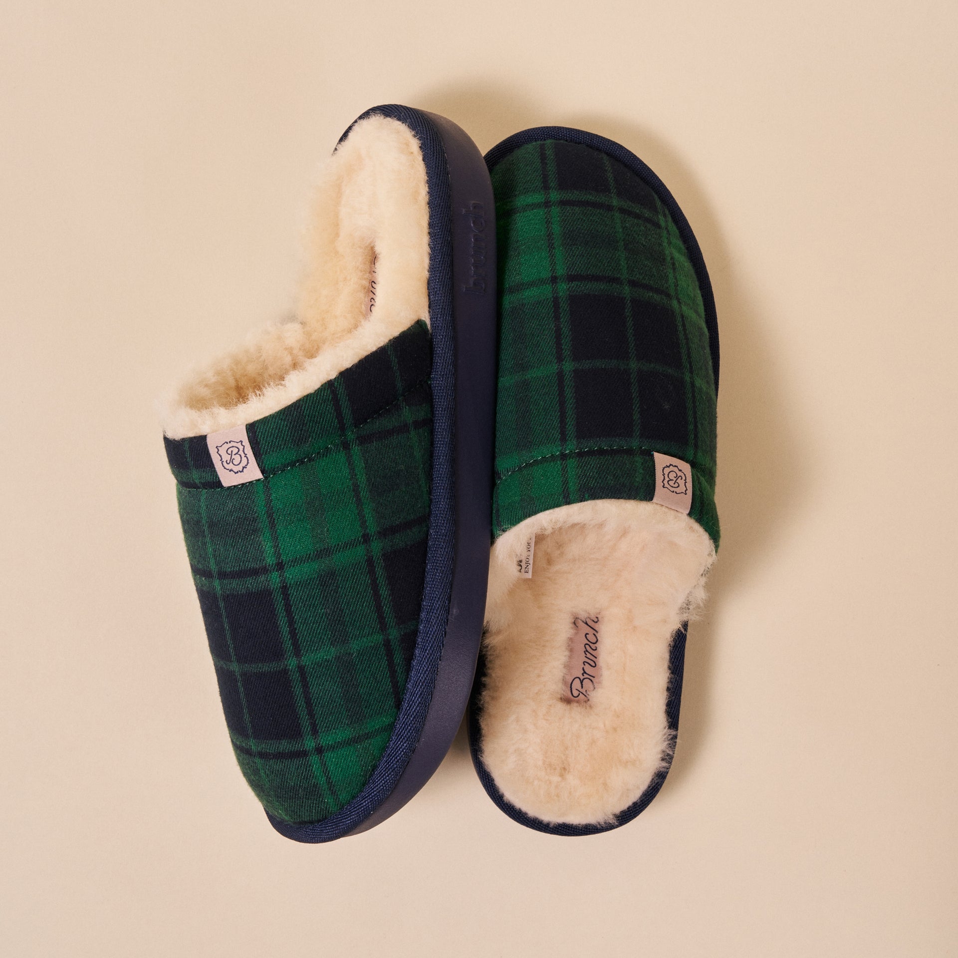 Green-and-navy plaid slip-on slippers with cream shearling lining and navy sole, brand tag reading 'Brunch'.