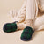 Green and navy tartan fleece-lined slippers on feet with cream cable‑knit pants and ribbed socks, set on beige background