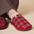 Red plaid slipper with brown sole on foot wearing cream ribbed sock, small tag showing B