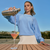 Woman in baby-blue sweatshirt pours pink cocktail from metal shaker into martini glass on wooden table at outdoor tennis court