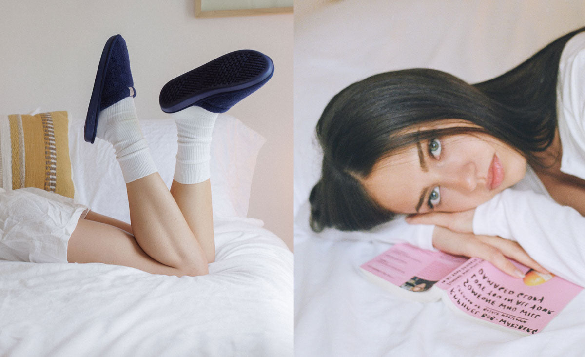 Woman lying on a bed, head on hands, with raised legs wearing navy slippers and white socks in a cozy bedroom scene