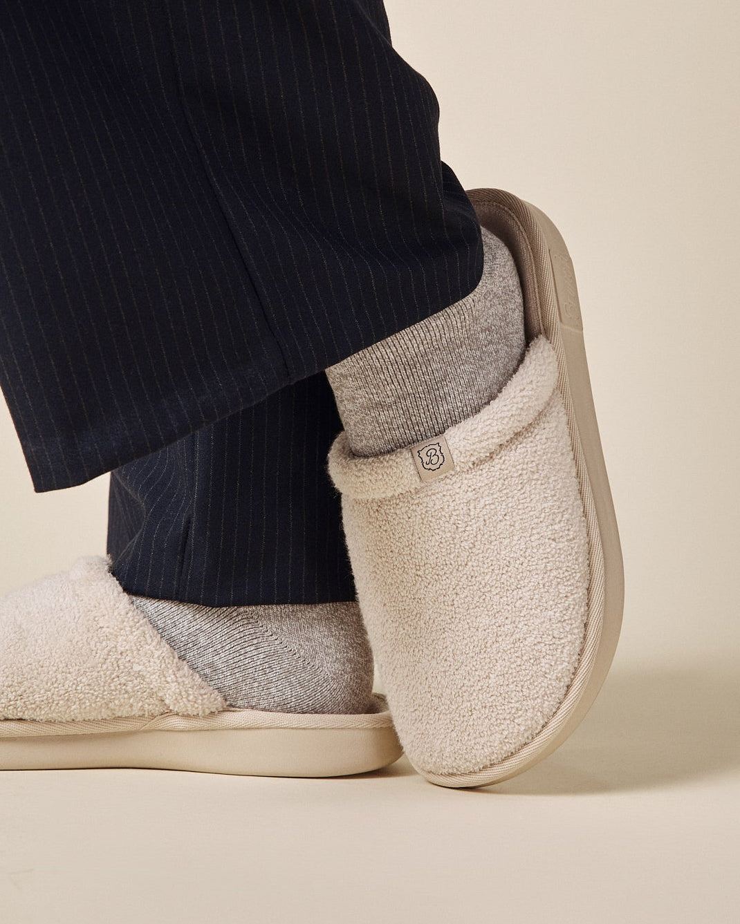 Beige slippers worn with dark pants and gray socks on a beige background