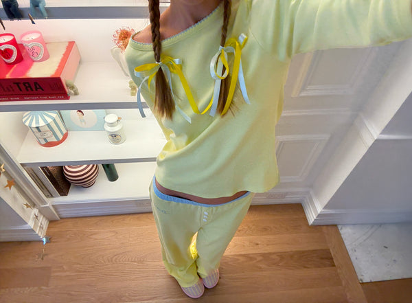 Person in yellow pajamas with braided pigtails tied by yellow and white ribbons, standing by shelves with decor; book labeled ART.