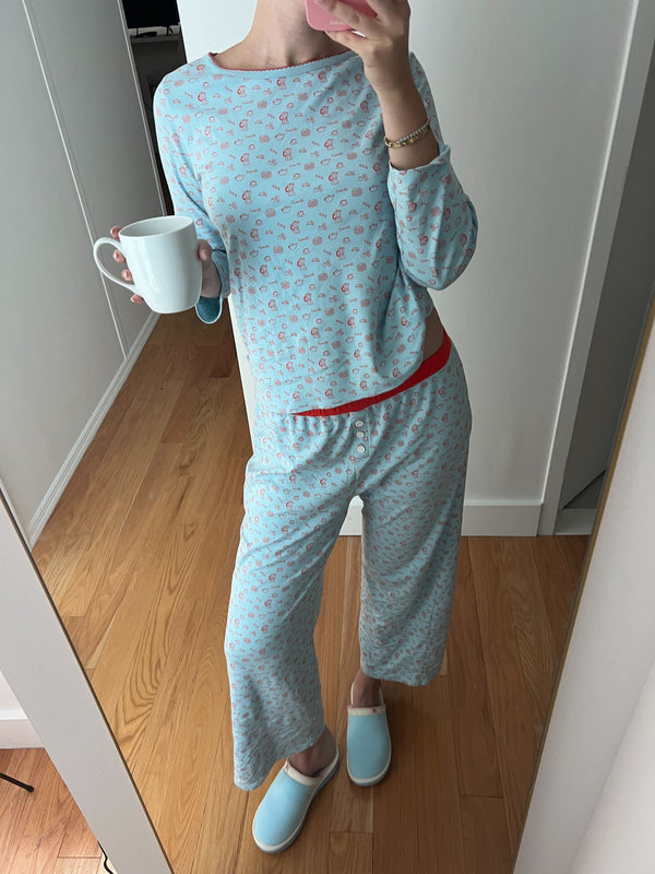 Person taking a mirror selfie wearing light blue patterned pajamas and matching slippers, holding a white mug