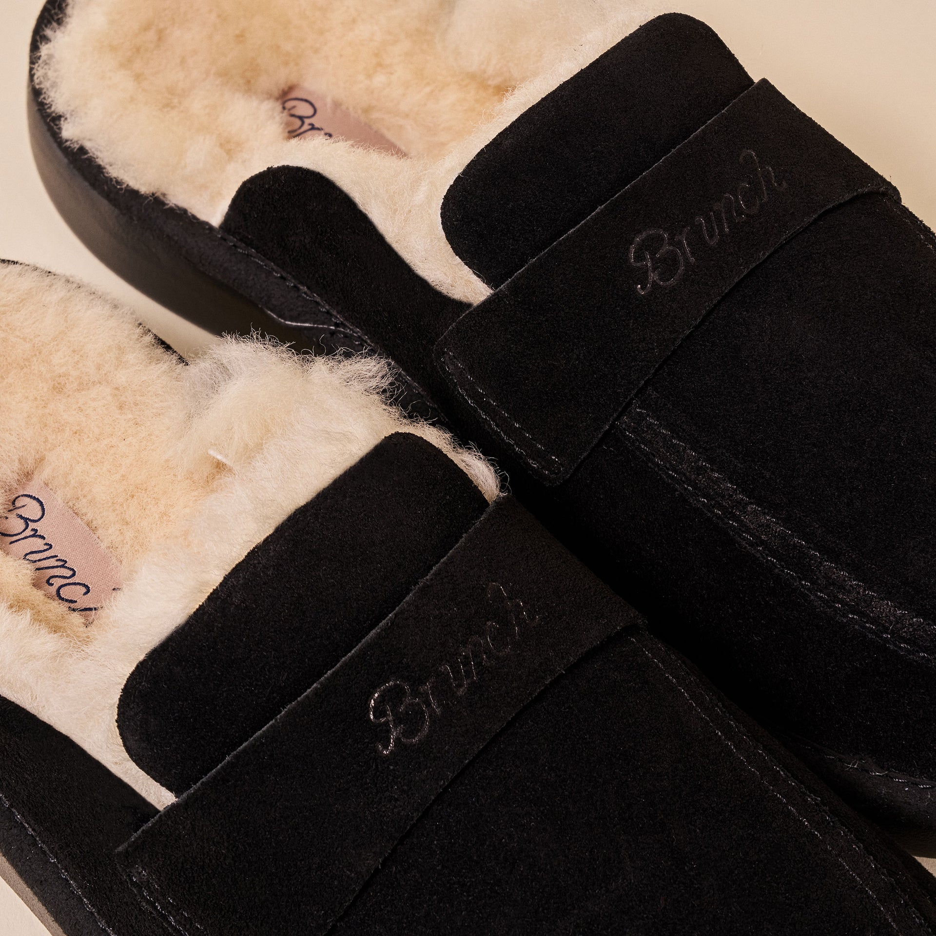 Black suede slippers with cream shearling lining, branded 'Brunch' embroidered on strap