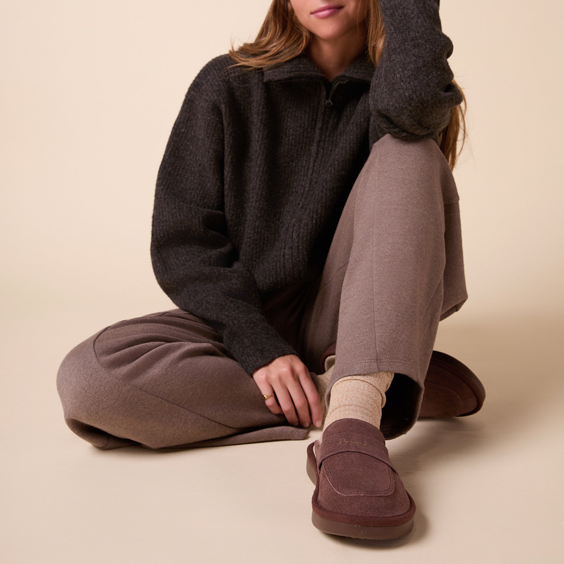 Seated person wearing charcoal pullover, mauve trousers and brown suede slip-on shoes