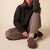 Seated person wearing charcoal pullover, mauve trousers and brown suede slip-on shoes