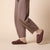 Brown suede backless loafer slippers worn with beige socks; cropped view of legs and pants