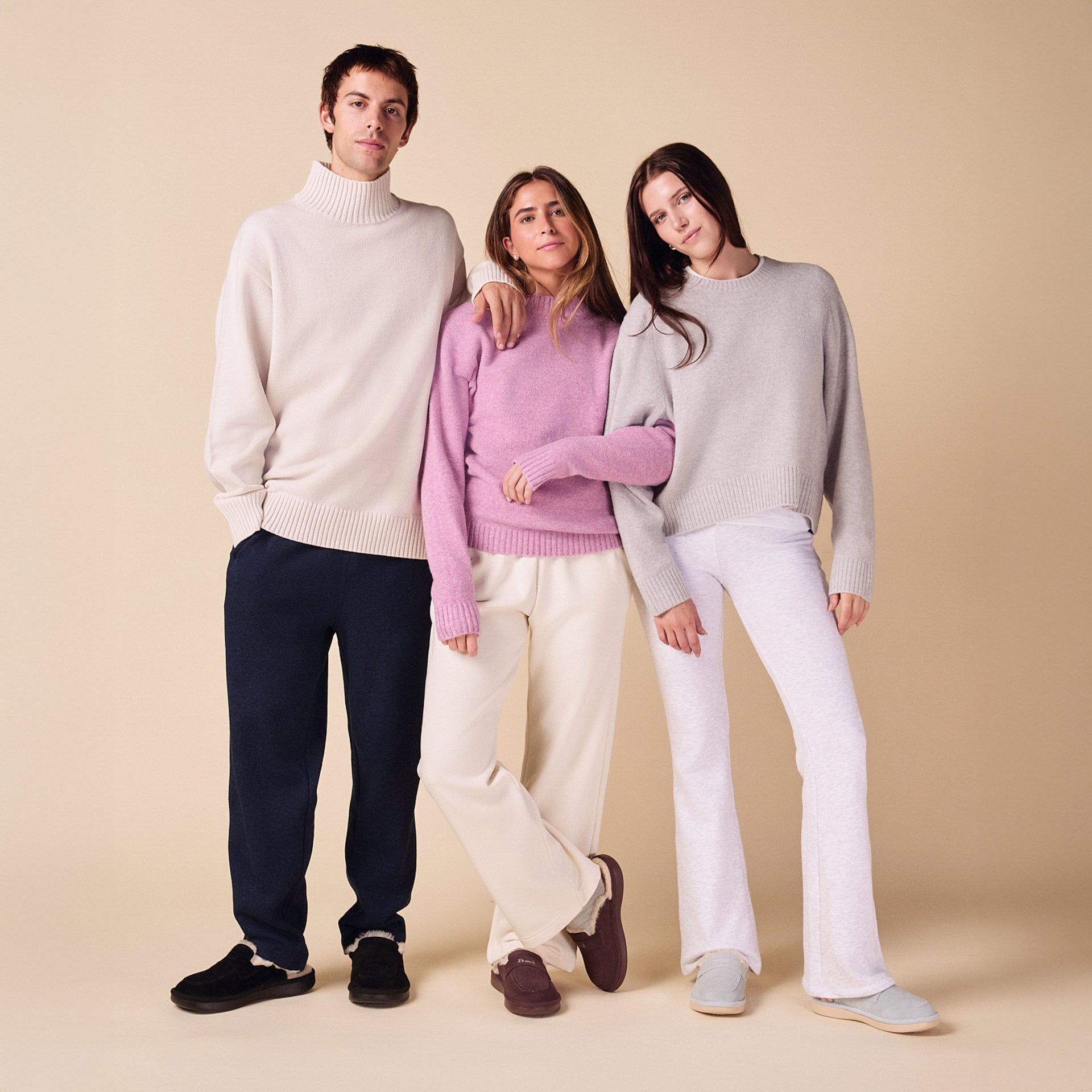 Three young adults in casual sweaters and lounge pants standing on beige background