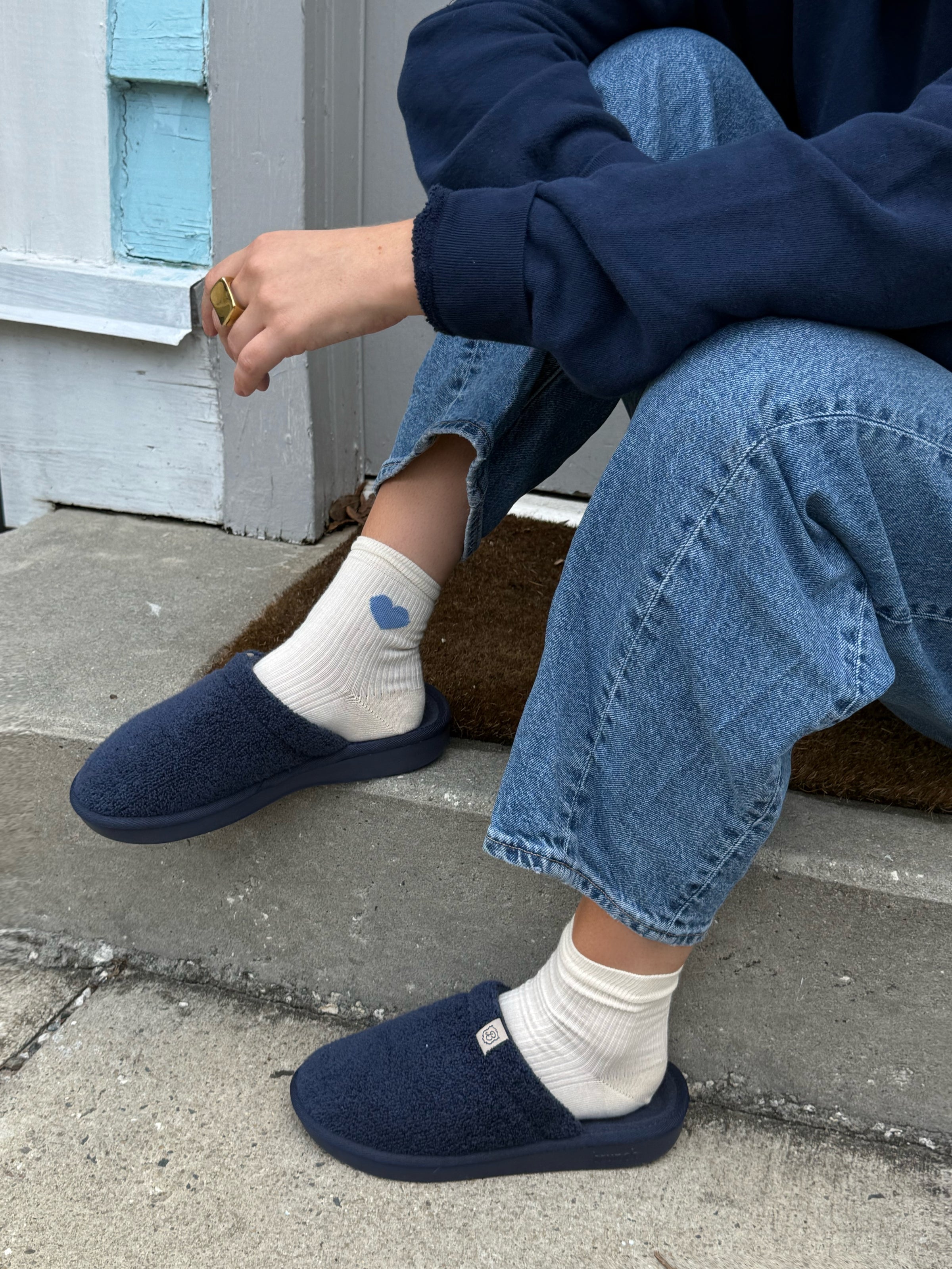 Person wearing navy slippers and light blue jeans sitting on a step.