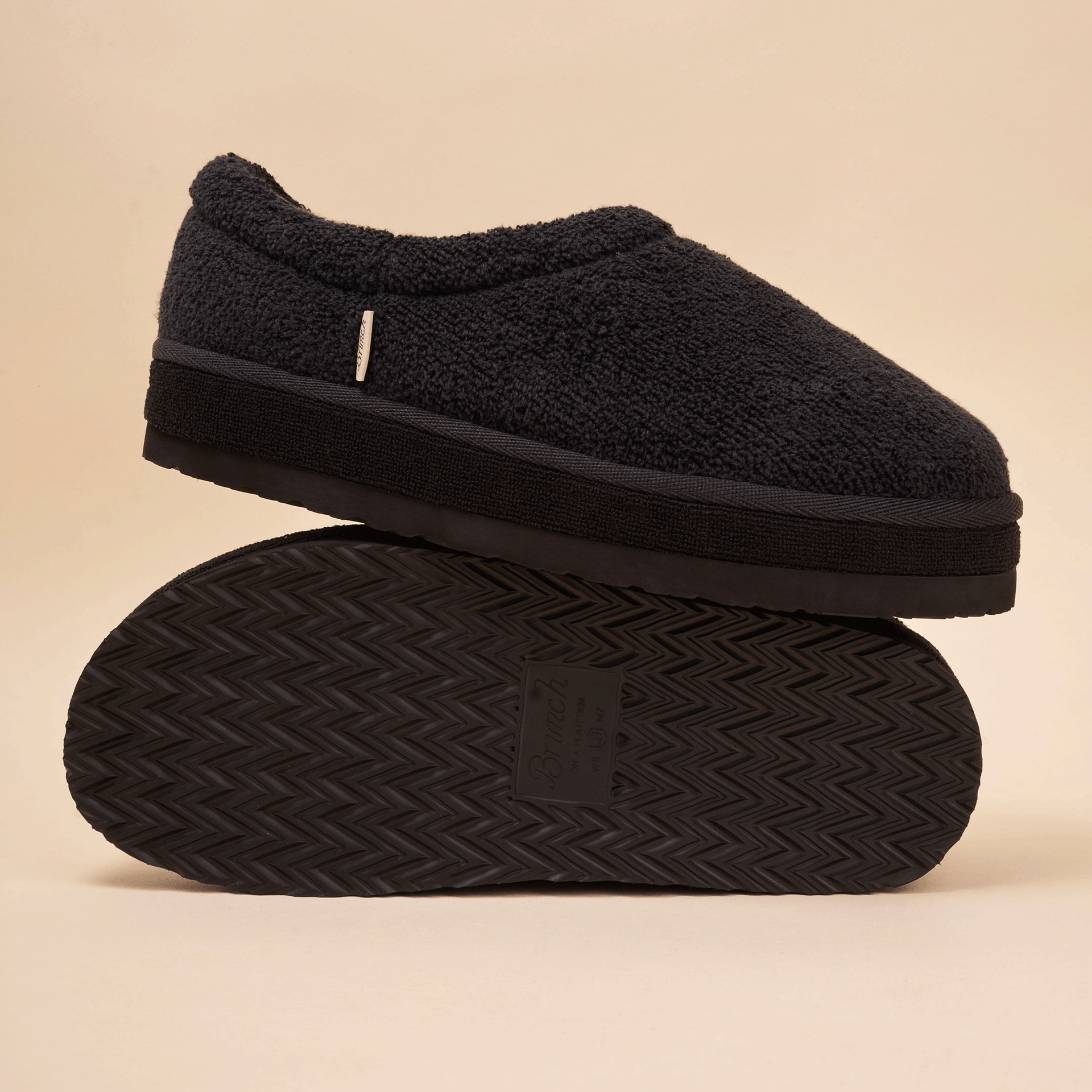 black sherpa slip-on slipper stacked on another to show plush upper and textured tread