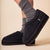 black fuzzy slip-on slippers with thick sole, shown on feet wearing gray socks