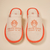Pair of beige spa slippers with orange trim embroidered 'THE WHITE LOTUS RESORT & SPA' and lotus logo