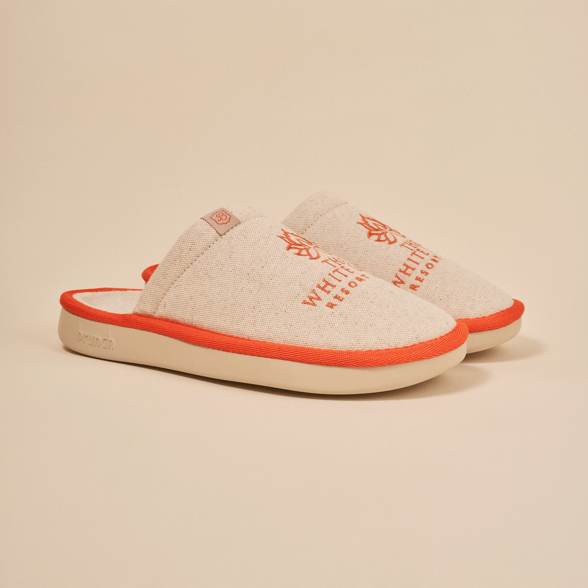 Beige slip-on slippers with orange trim, embroidered 'THE WHITE RESORT', small tag 'B' and embossed 'brunch' on the sole.