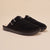 Front three-quarter view of Amour Shearling slip-on mule in black suede showcasing shearling lining, adjustable side buckle, and Brunch-branded sole on beige background