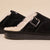 Side view of Amour Shearling slipper in black suede with cream lining, adjustable buckle, and Brunch logo on sole