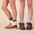Three-quarter view of Apres Boot in camel nubuck on models' feet showcasing folded shearling cuff and low-profile sole on beige studio background