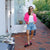 Woman standing outside a storefront labeled ALV JEWELS at Brunch, wearing a bright pink cardigan and brown shoes with pink laces, balloons and hydrangeas in the background