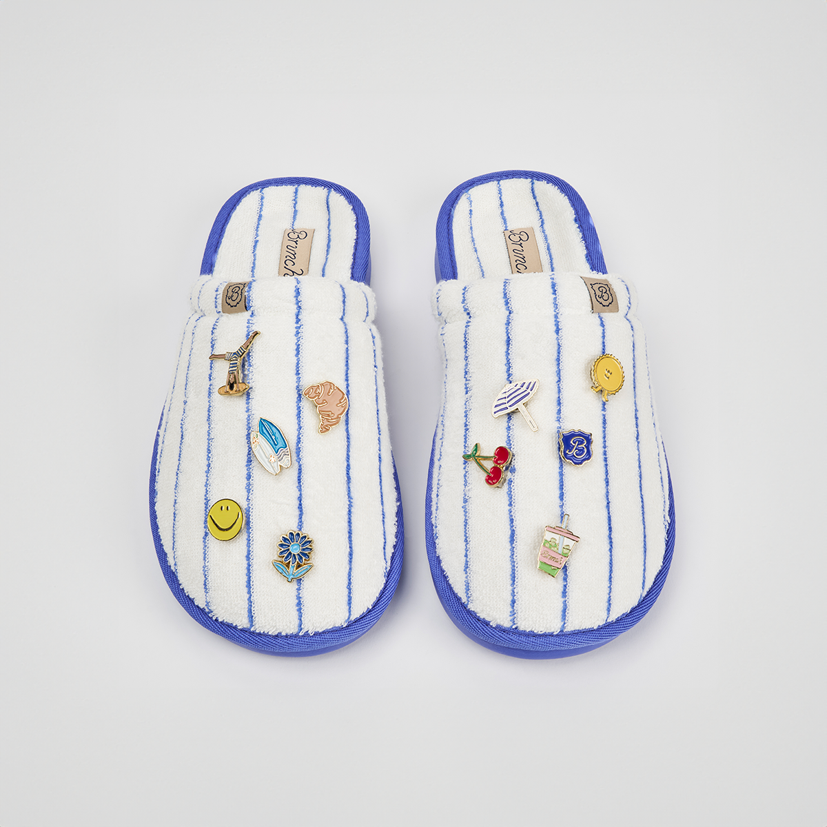 Top view of Essential Regatta striped terry slippers with blue pinstripes, purple trim and magnetic charms on white