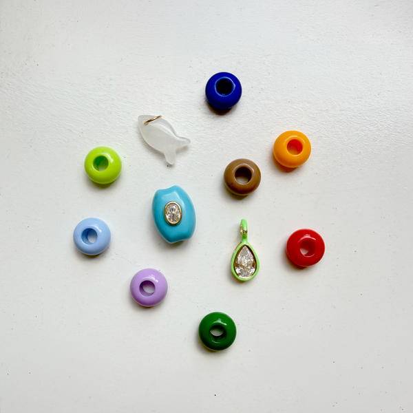 Top-down view of Carrie Charm Kit showing multicolor donut beads, a white fish charm, and turquoise and green rhinestone charms on a white background