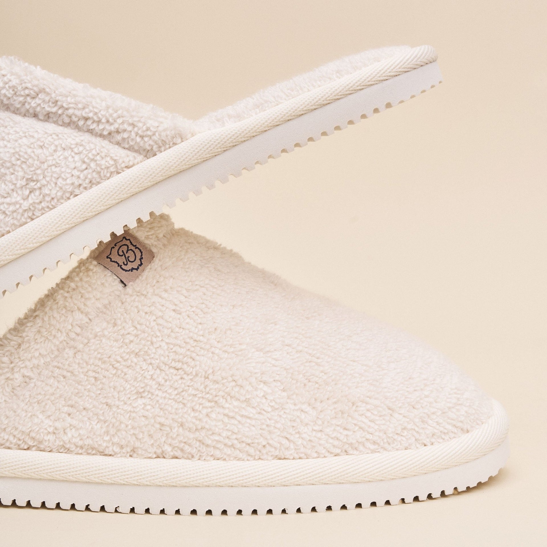 Close-up side view of Classic cream terry slipper showcasing soft terry upper and serrated Vibram sole on beige background