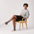 Model seated in a wooden chair wearing cream terry Classic slippers with a slim profile and gray socks on a light studio background