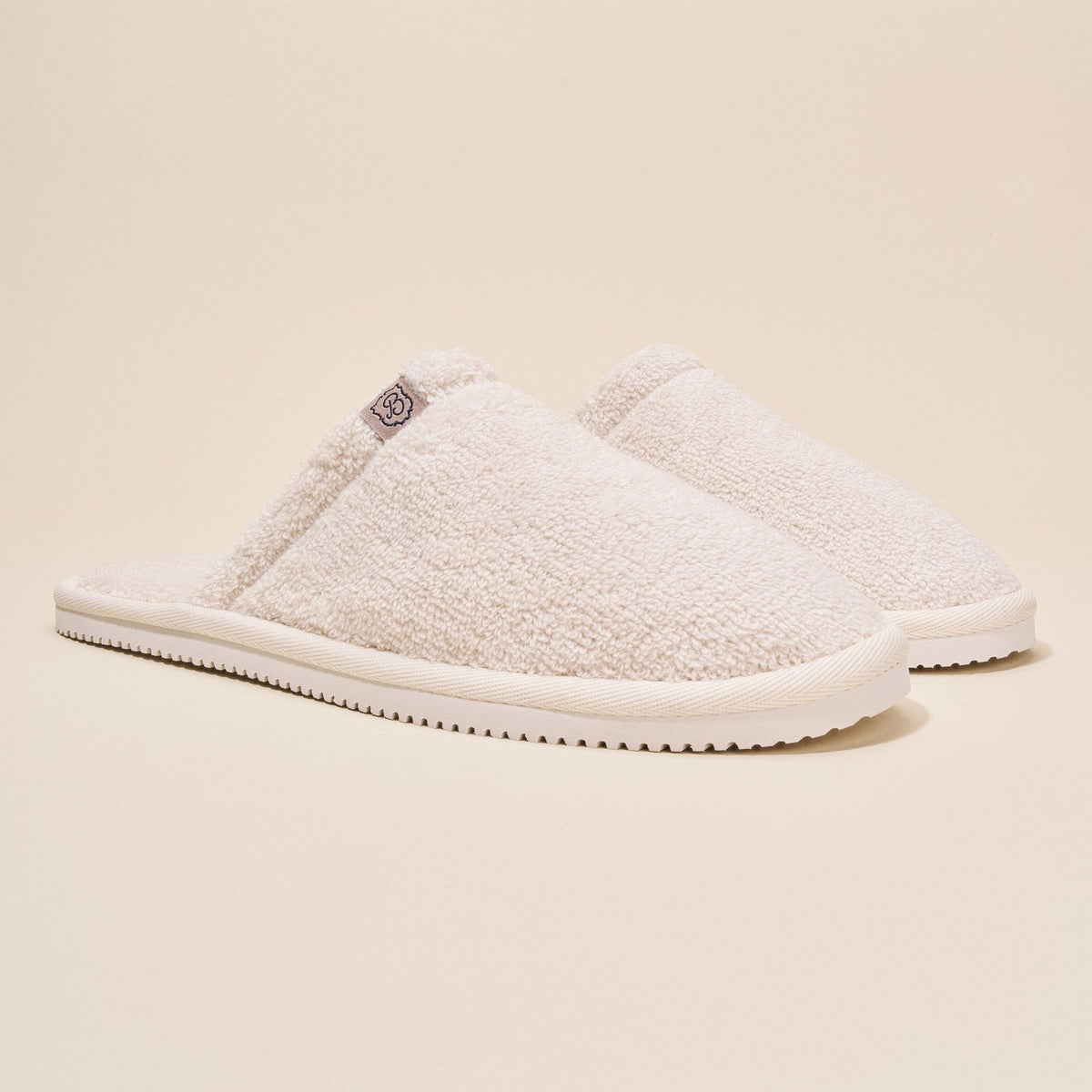Three-quarter side view of Classic Cream Terry Slipper showcasing cream terry upper and slim white sole on beige background