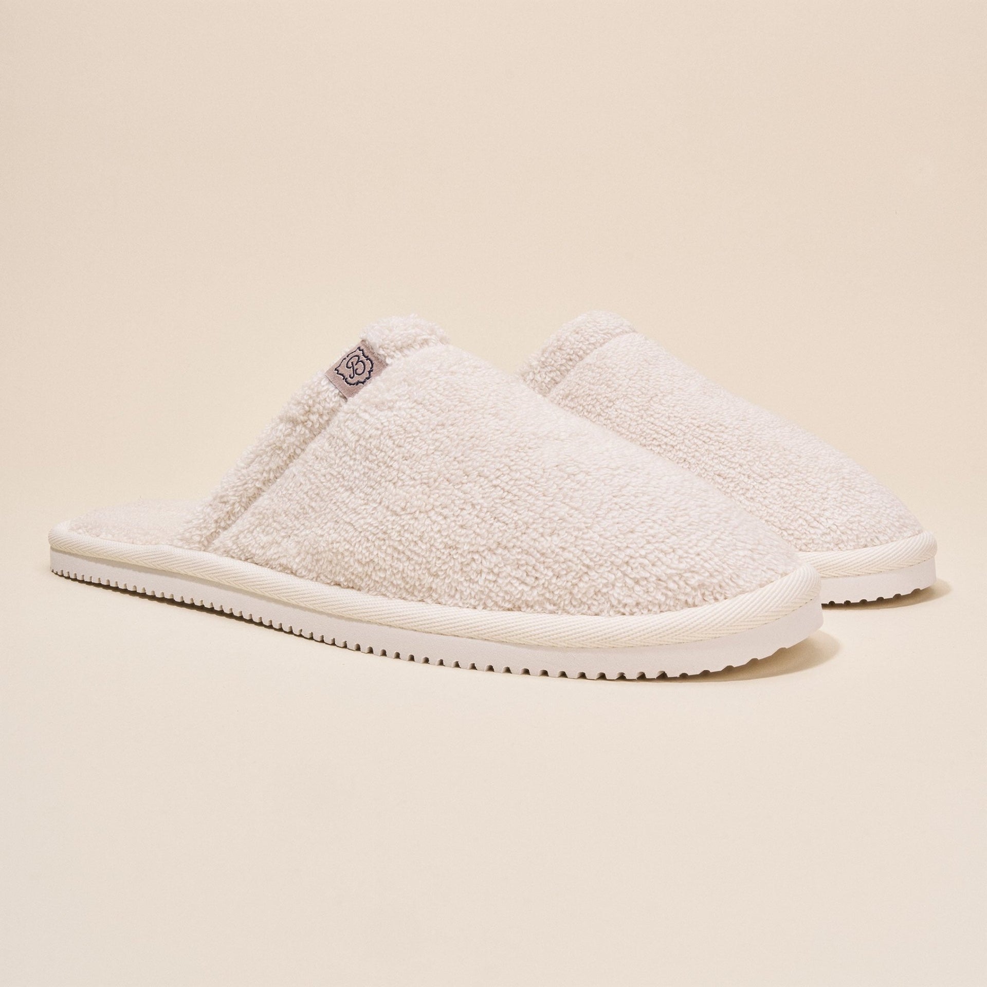 Three-quarter side view of Classic Cream Terry Slipper showcasing cream terry upper and slim white sole on beige background