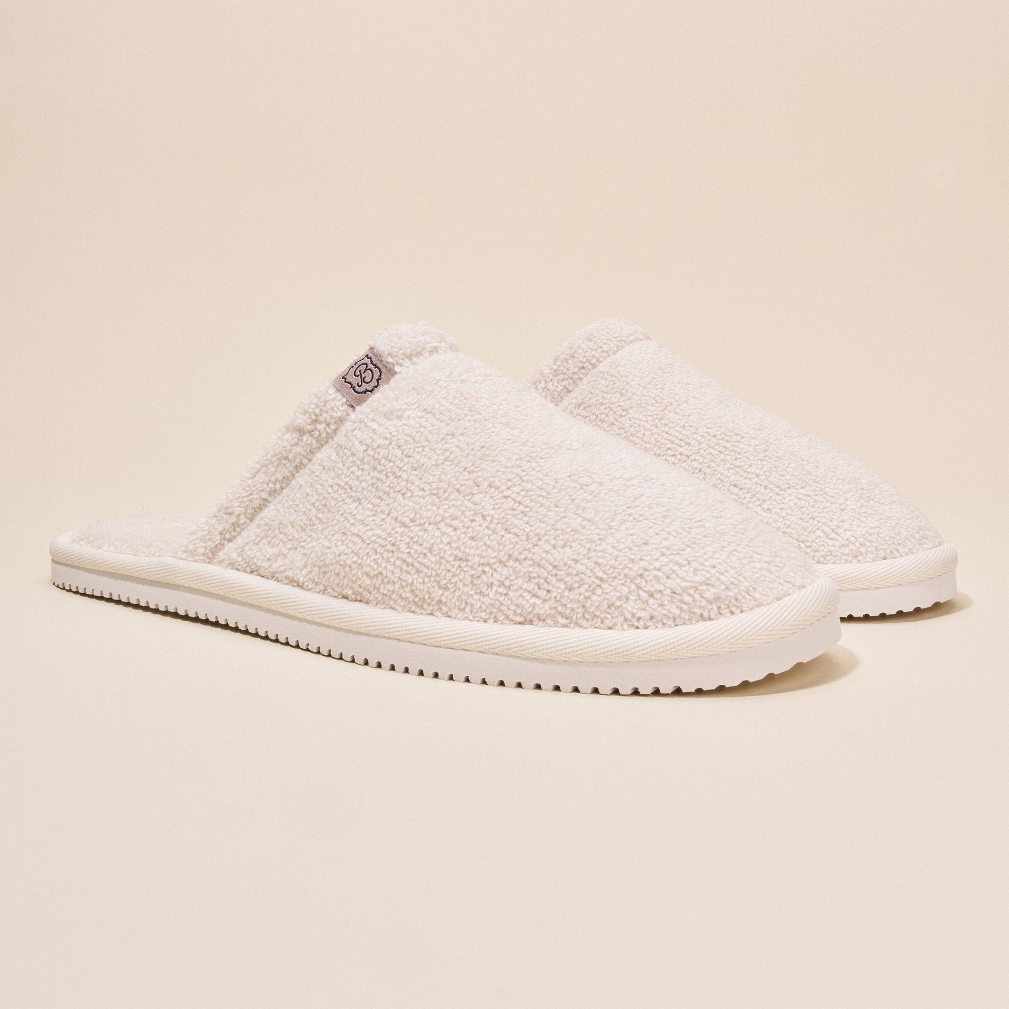 Three-quarter side view of Classic Cream Terry Slipper showcasing cream terry upper and slim white sole on beige background