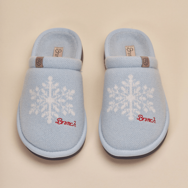 Top view of Essential Cashmere slippers in blue showing white snowflake knit pattern, red Brunch embroidery and leather logo tab on a beige background