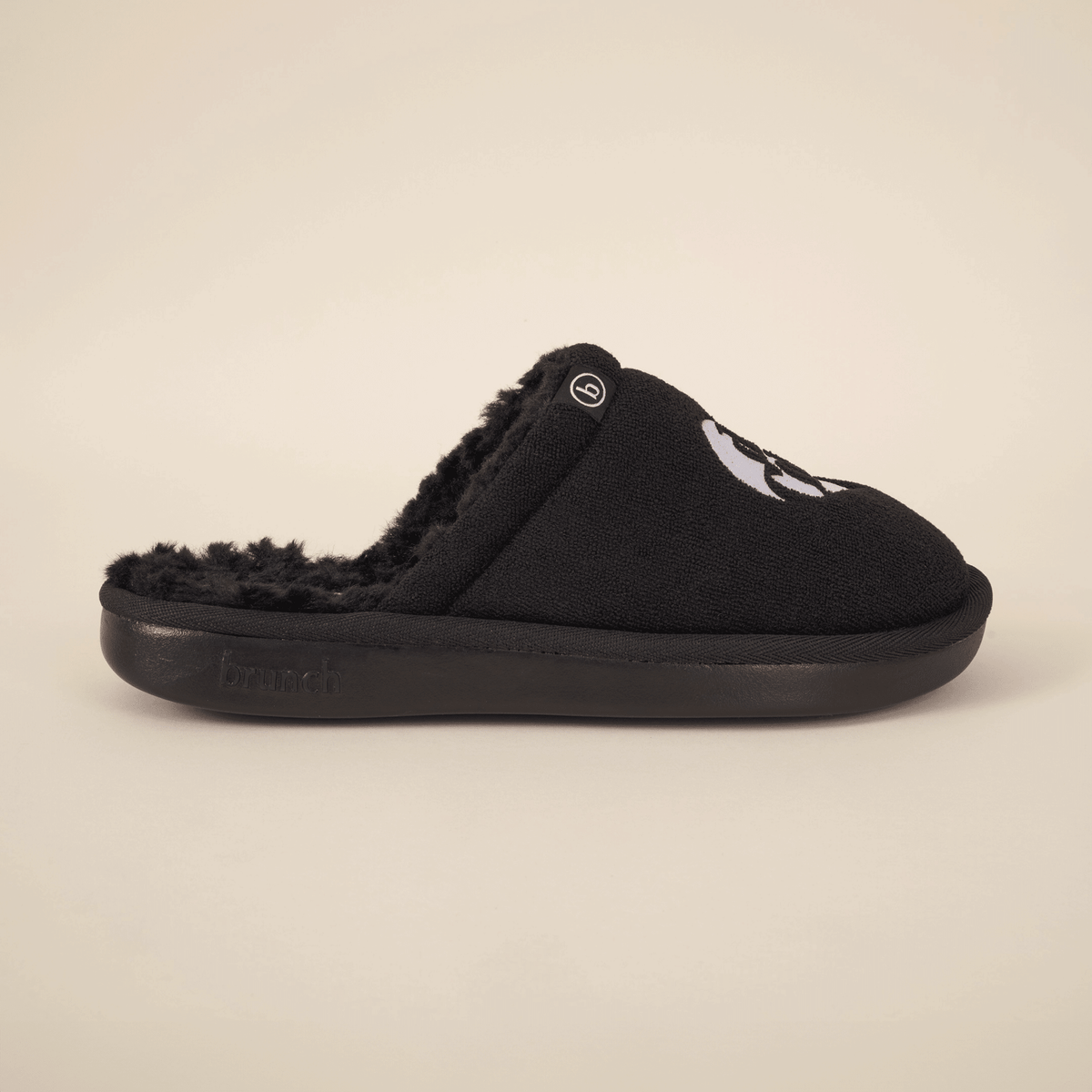 Side view of black Diet Coke x Brunch slipper with faux shearling lining and embroidered logo on beige background
