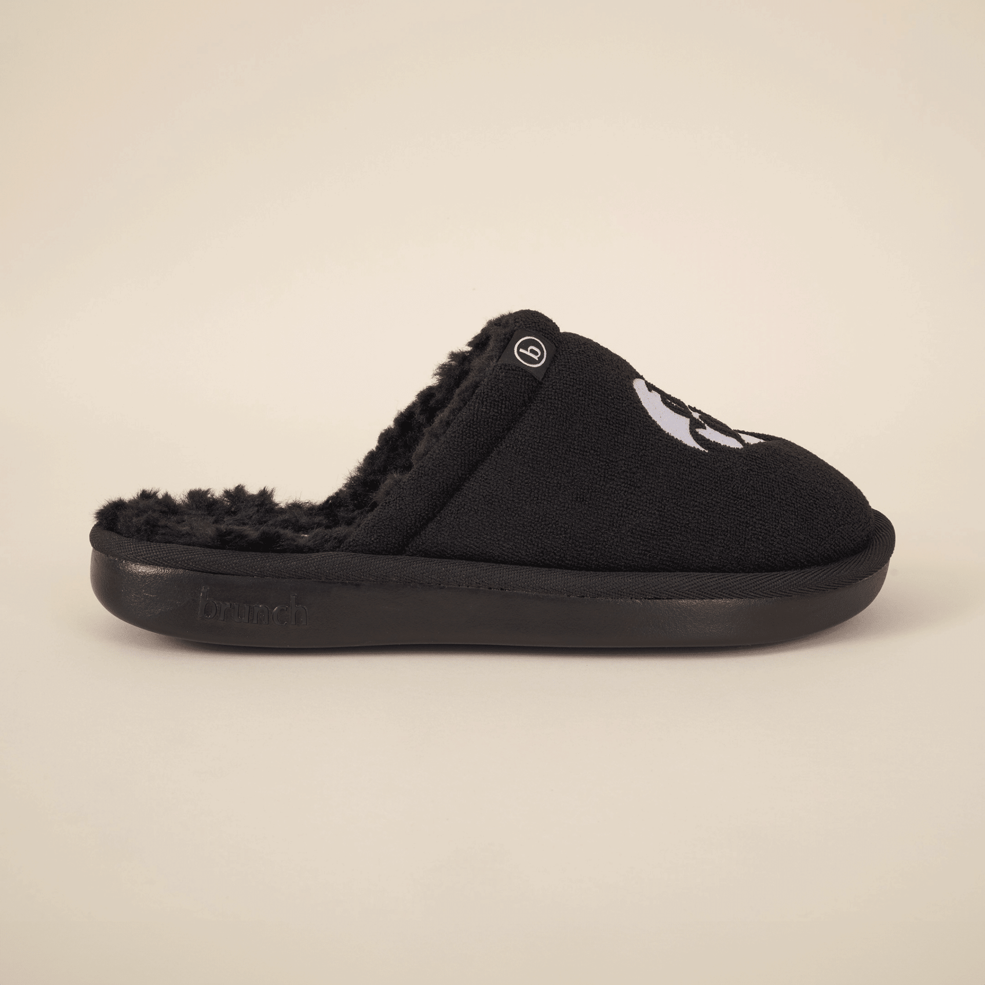 Side view of black Diet Coke x Brunch slipper with faux shearling lining and embroidered logo on beige background