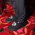 Front view of black slip-on shearling slippers showcasing white heart Diet Coke logo embroidered on top with red star-pattern carpet background