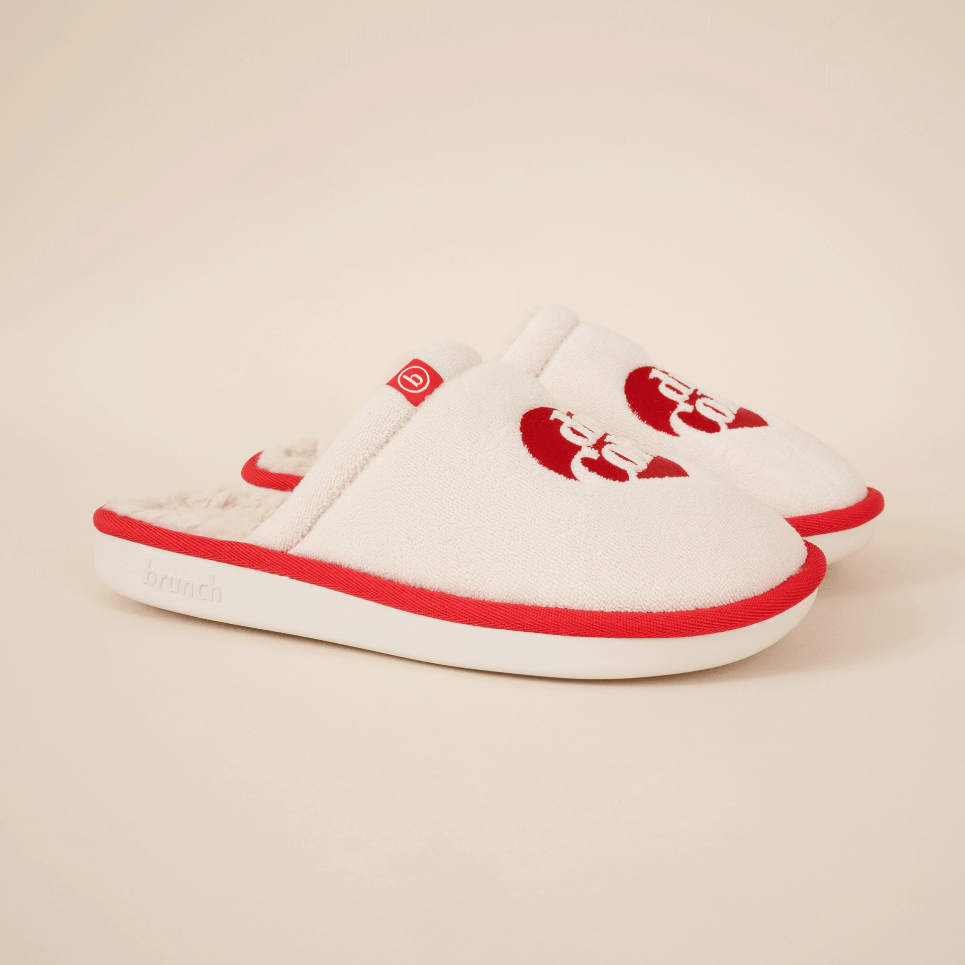 Three-quarter view of cream slip-on slippers showing red Diet Coke logo, red piping and faux-shearling lining on beige