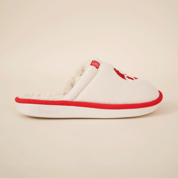 Side view of Diet Coke shearling slipper showing cream upper, faux shearling lining, red trim and white sole on neutral background