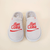 Top-down view of grey shearling slippers with red embroidered diet Coke logo on beige background